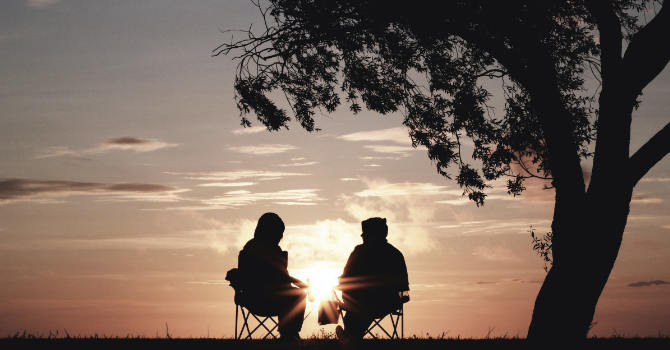 Two friends sitting in the park at sunset